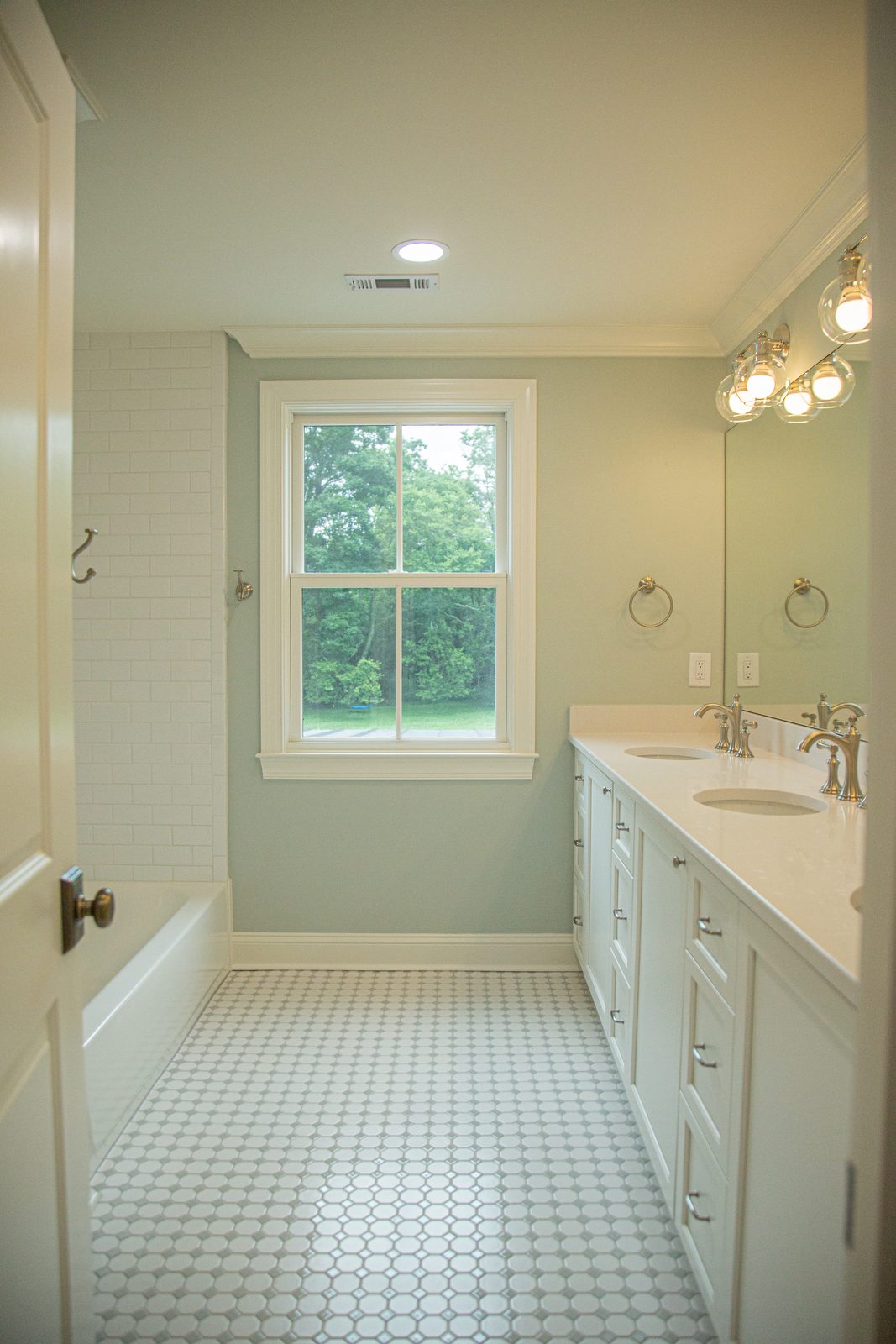 Renovated bathroom with sage walls, a double vanity, and a hex tile floor
