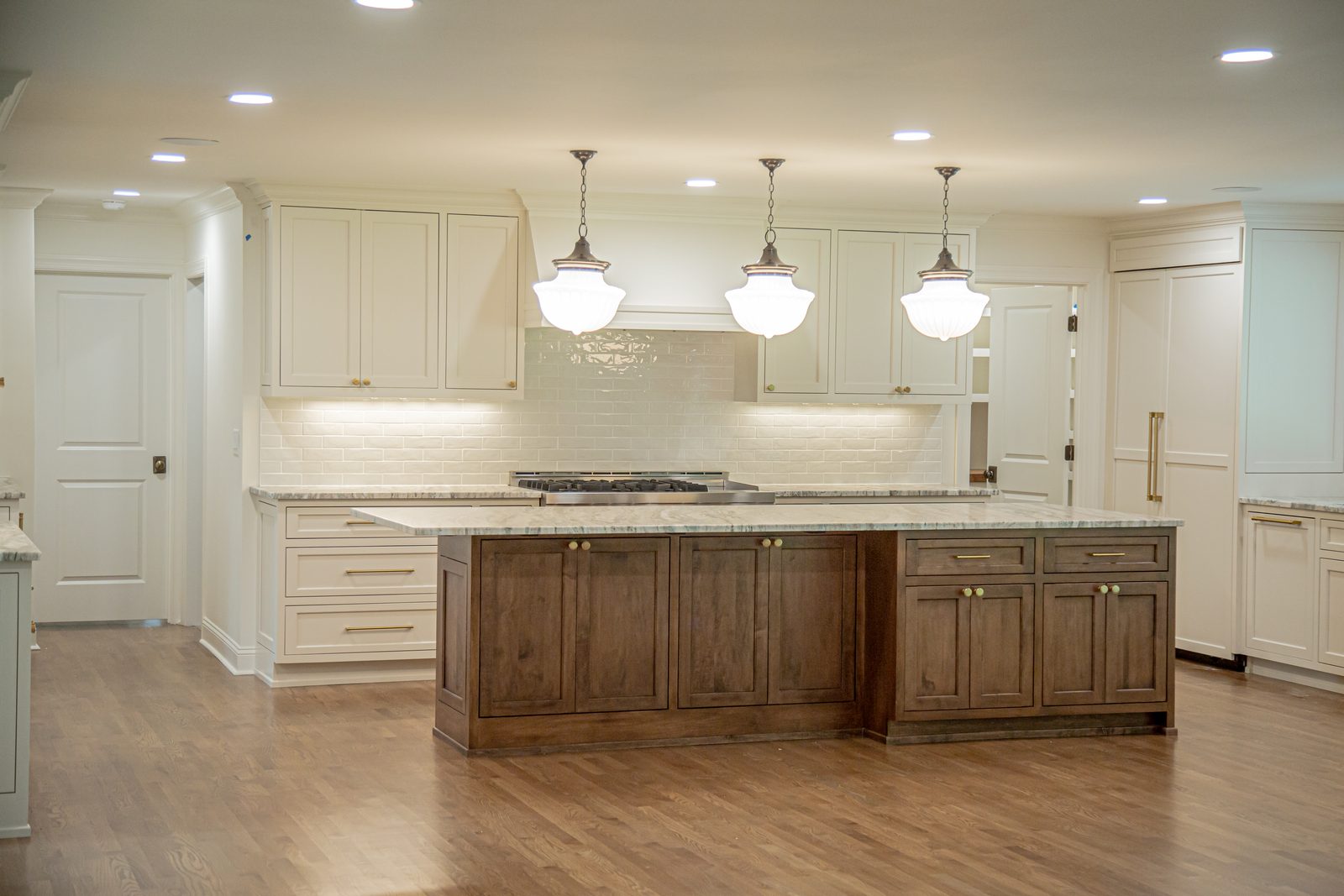 Custom kitchen with cream cabinetry, a walnut island, and schoolhouse pendants
