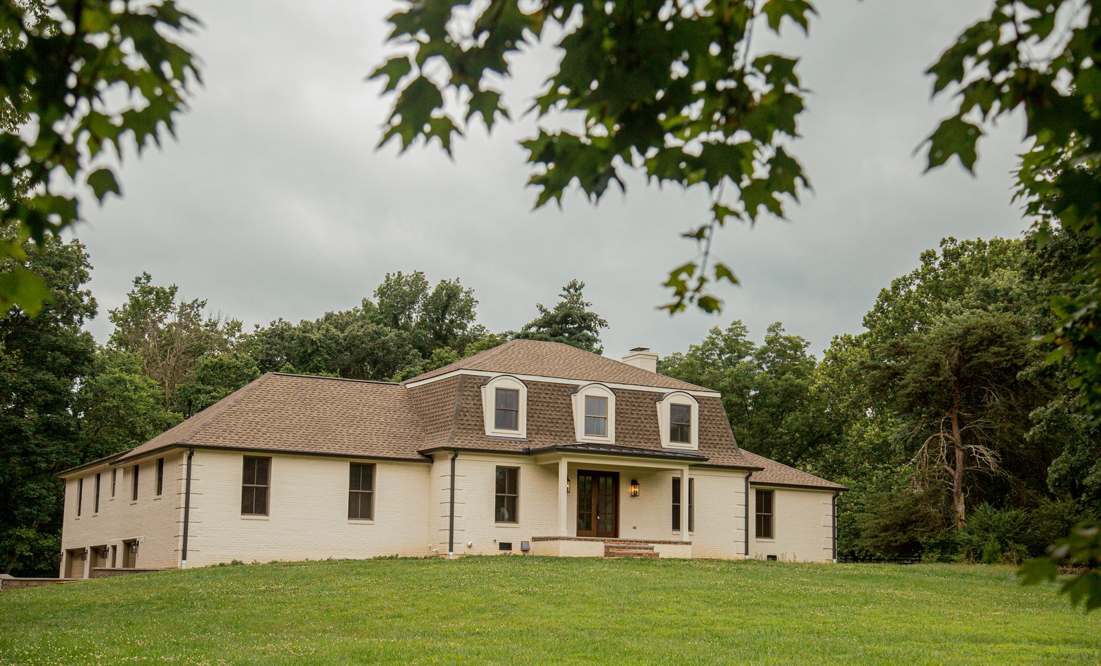 Estate home exterior with a gambrel roof, dormer windows, and a covered entry