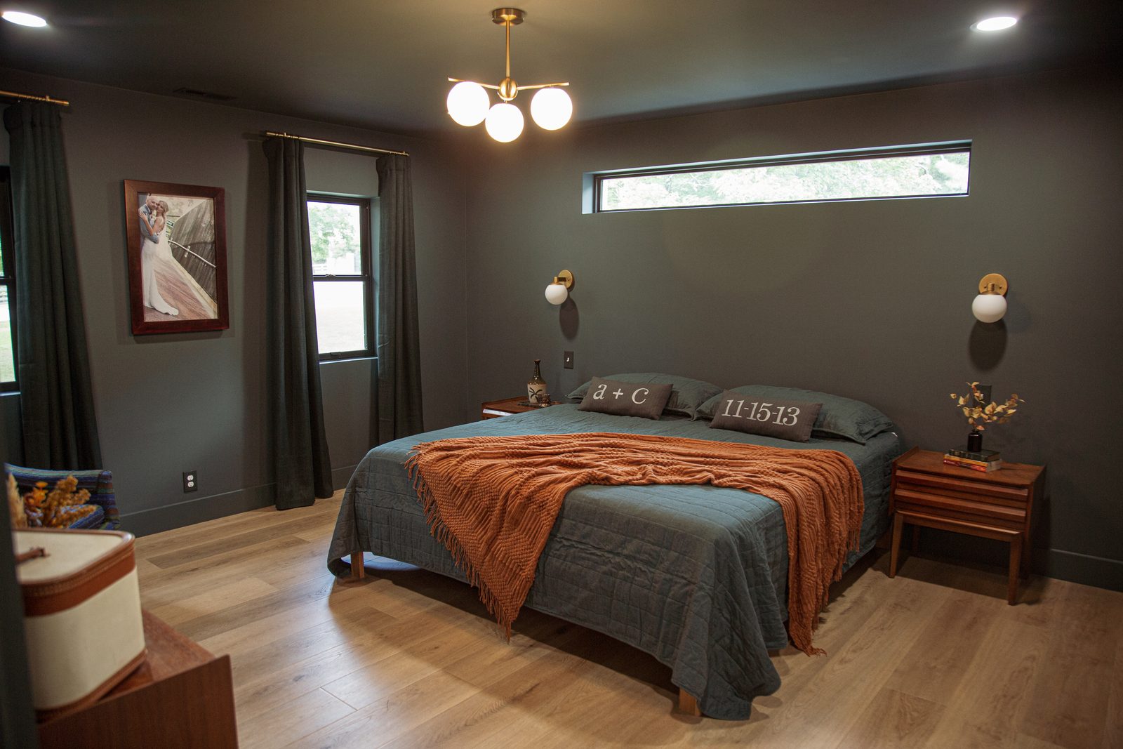 Primary bedroom with deep charcoal walls, warm wood nightstands, and a clerestory window